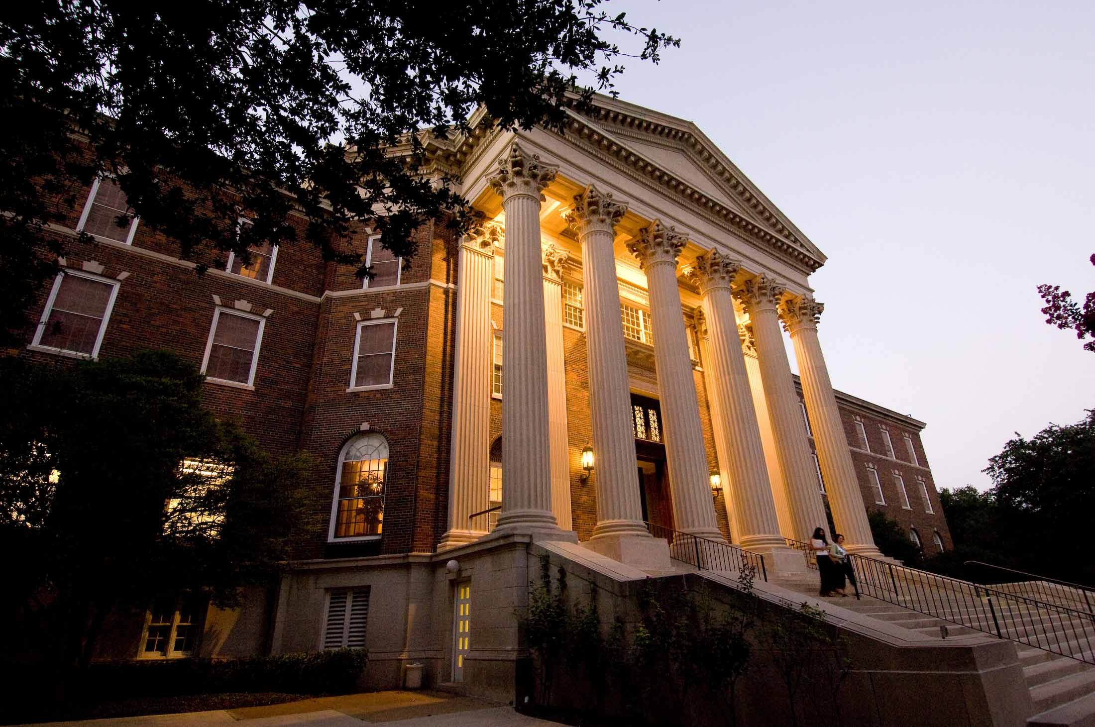 Two students walking down the lit staircase of SMU's Dallas Hall at dusk