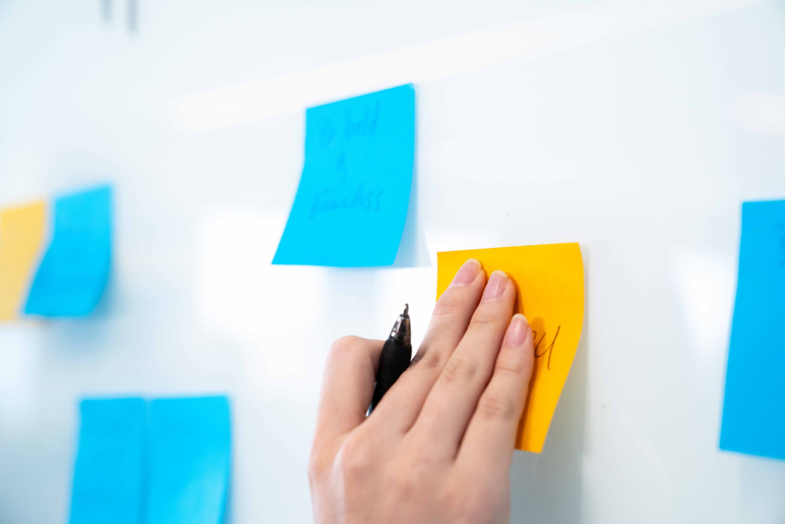 A hand holding a pen puts a sticky note on a whiteboard