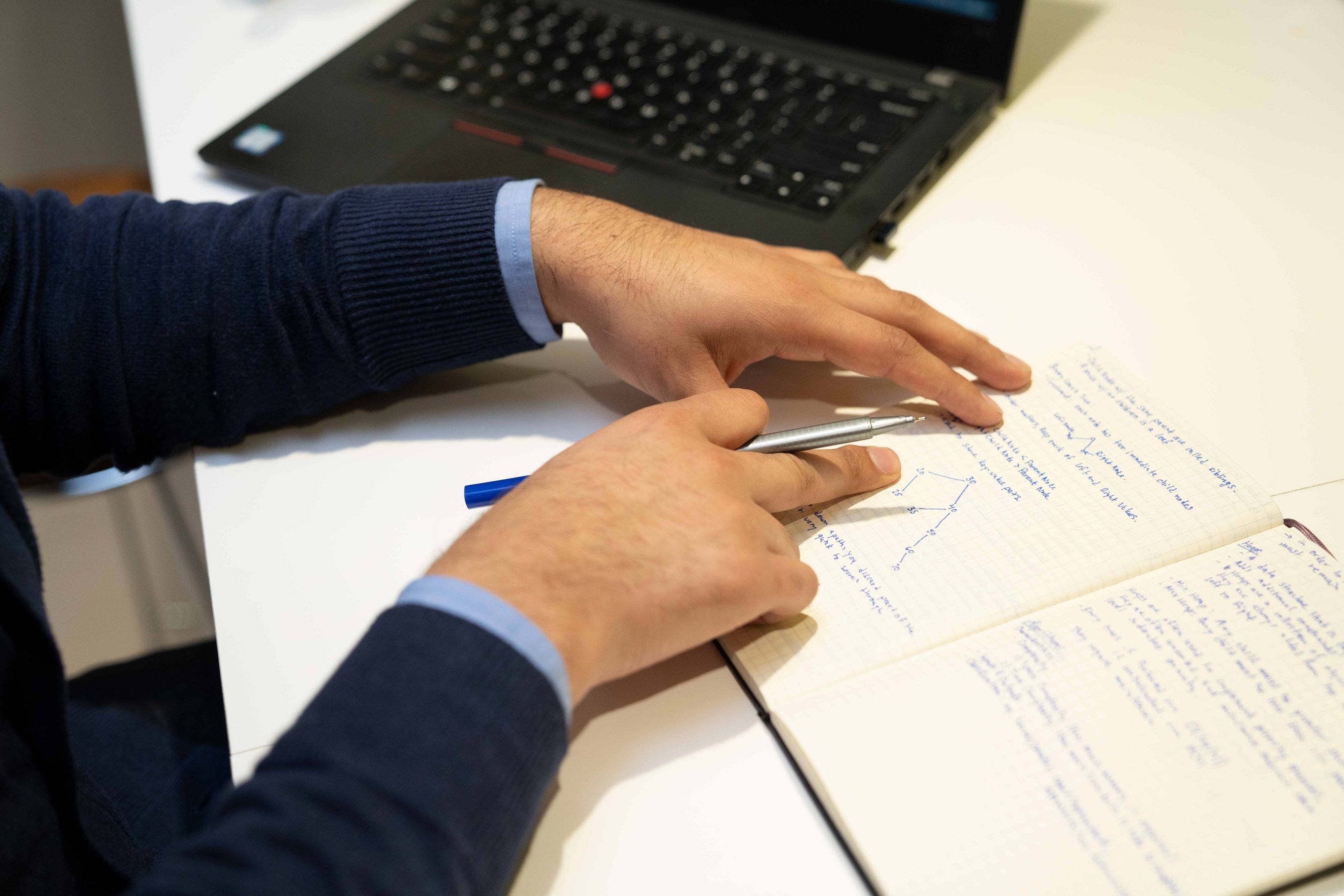 Man in blue sweater reviews notes with a pen to make edits