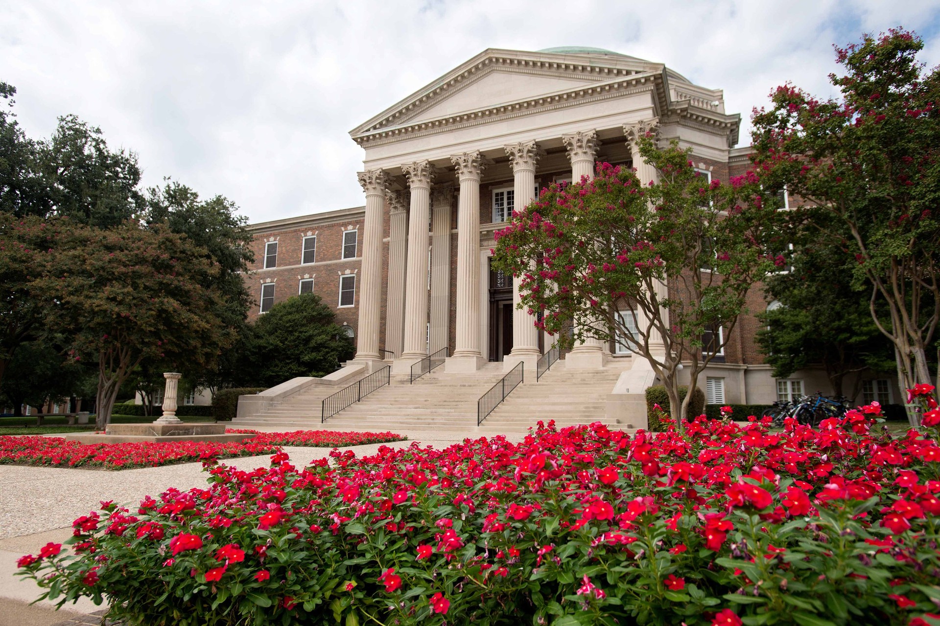 A view from the side of the stairs walkway lined with red flowering plants to Dallas Hall at SMU