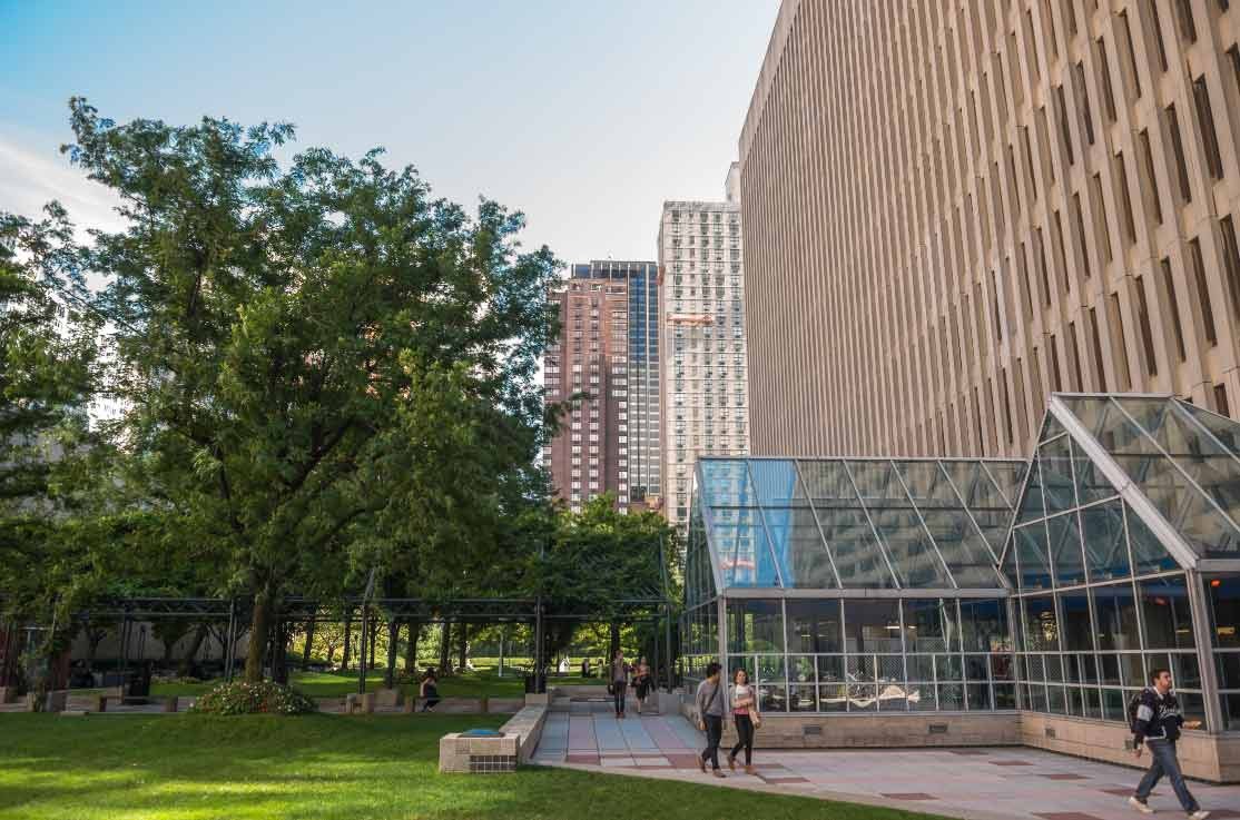 Students walk near a grassy quad next to an academic building at Fordham University